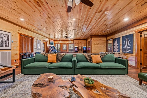 Spacious wood-paneled living room with green sectional sofa, live-edge wood coffee table, and ceiling fan